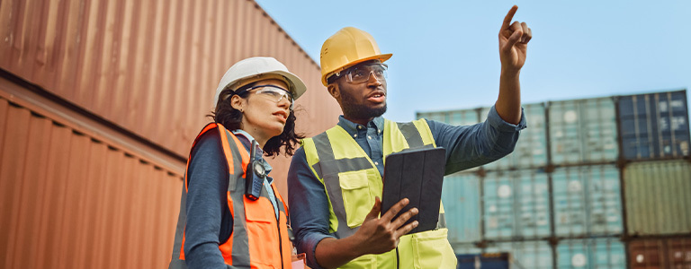 Man in hard hat and reflective vest holding ipad and talking with woman in construction uniform