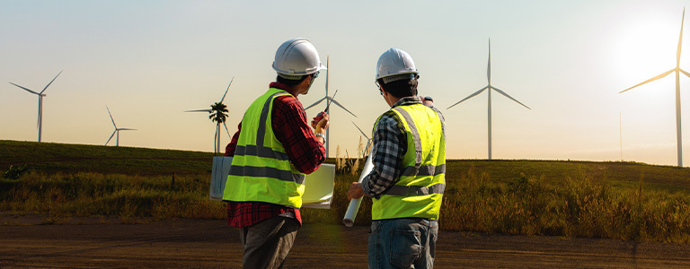 image of two wind turbine technicians discussing plans with backdrop of wind turbines