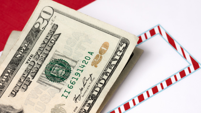 small stack of twenty-dollar bills sitting on an envelope with a candy cane pattern, indicating holiday gift challenges