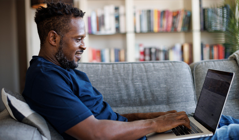 Man at home on couch with laptop, smiling